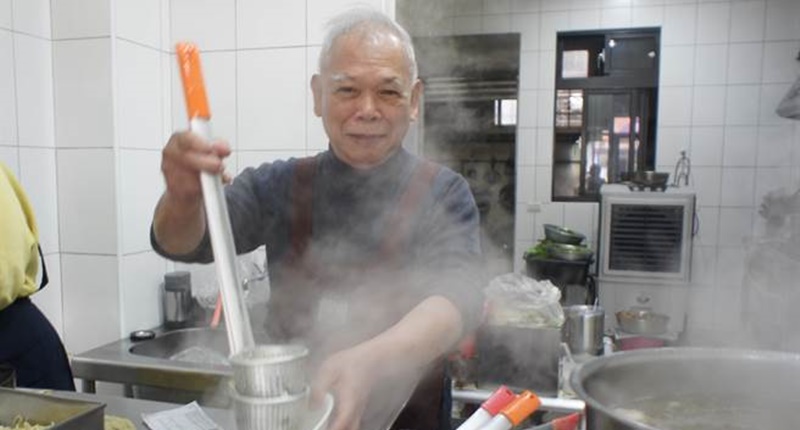 「麵哥麵嫂」第二代老闆江文雄自父親手上接下麵攤,汆燙麵條時習慣以塑膠碗敲麵簍發出叩叩叩的聲音,已是店裡習以為常的背景音。(馮惠宜攝)
