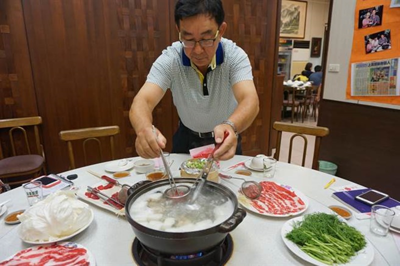張集光示範北京涮羊肉吃法,他將生羊肉放進撈網內,以滾燙熱湯涮成粉紅色,即可入口食用。(王文吉攝)
